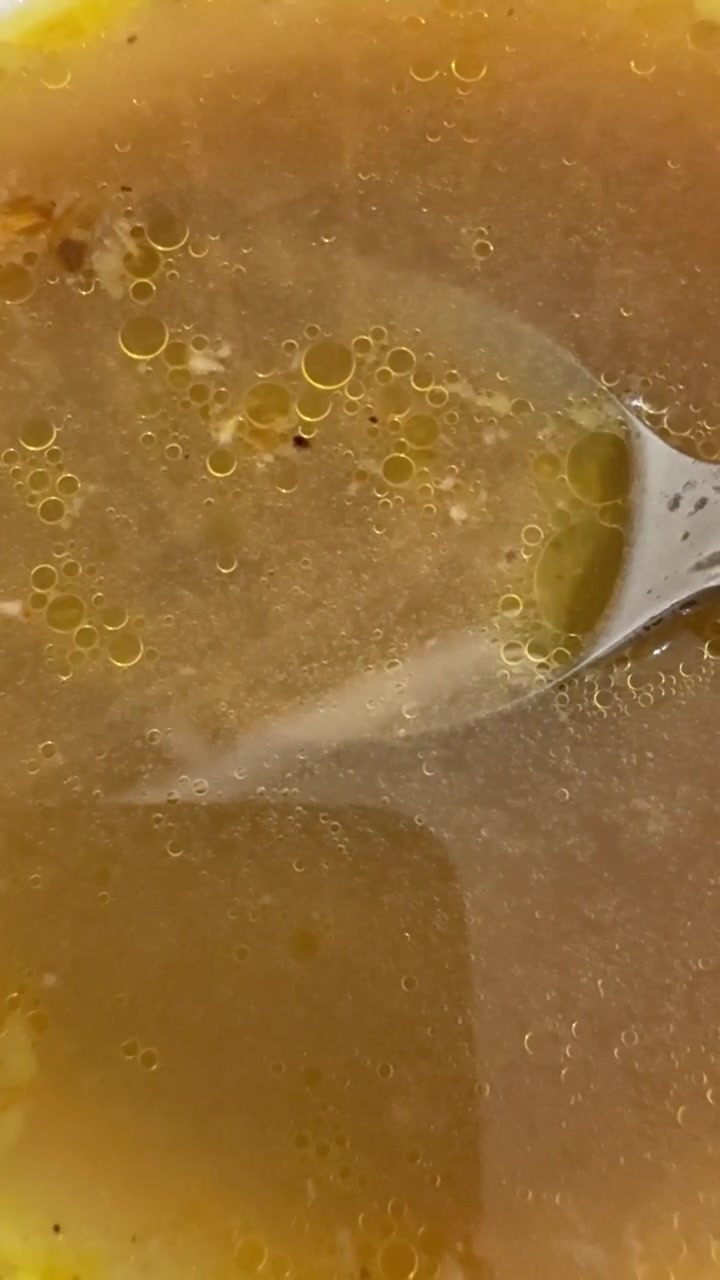Primo piano di un cucchiaio di metallo appoggiato in una ciotola di brodo.