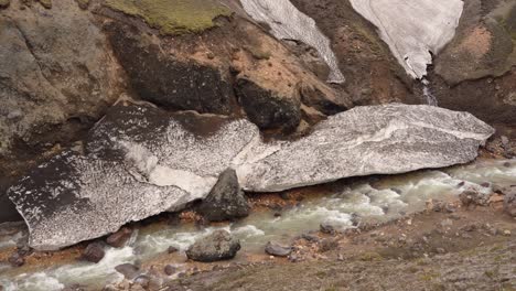 vista fija del río que desciende de brennisteinsalda en landmannalaugar, islandia, con un bloque de nieve a lo largo de la orilla del río