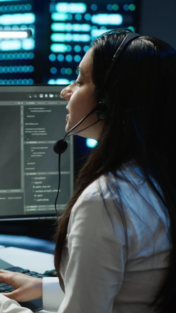 Donna che indossa una cuffia mentre parla e lavora al computer in un ufficio buio