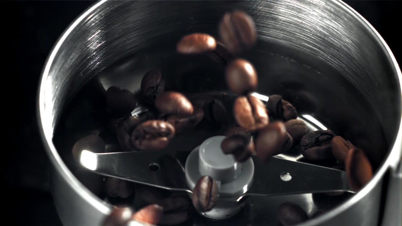 Chicchi di caffè che cadono in un macinacaffè elettrico al rallentatore