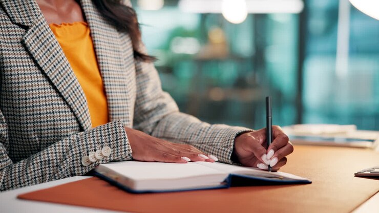 Professional Woman Writing Notes in a Notebook at Her Desk