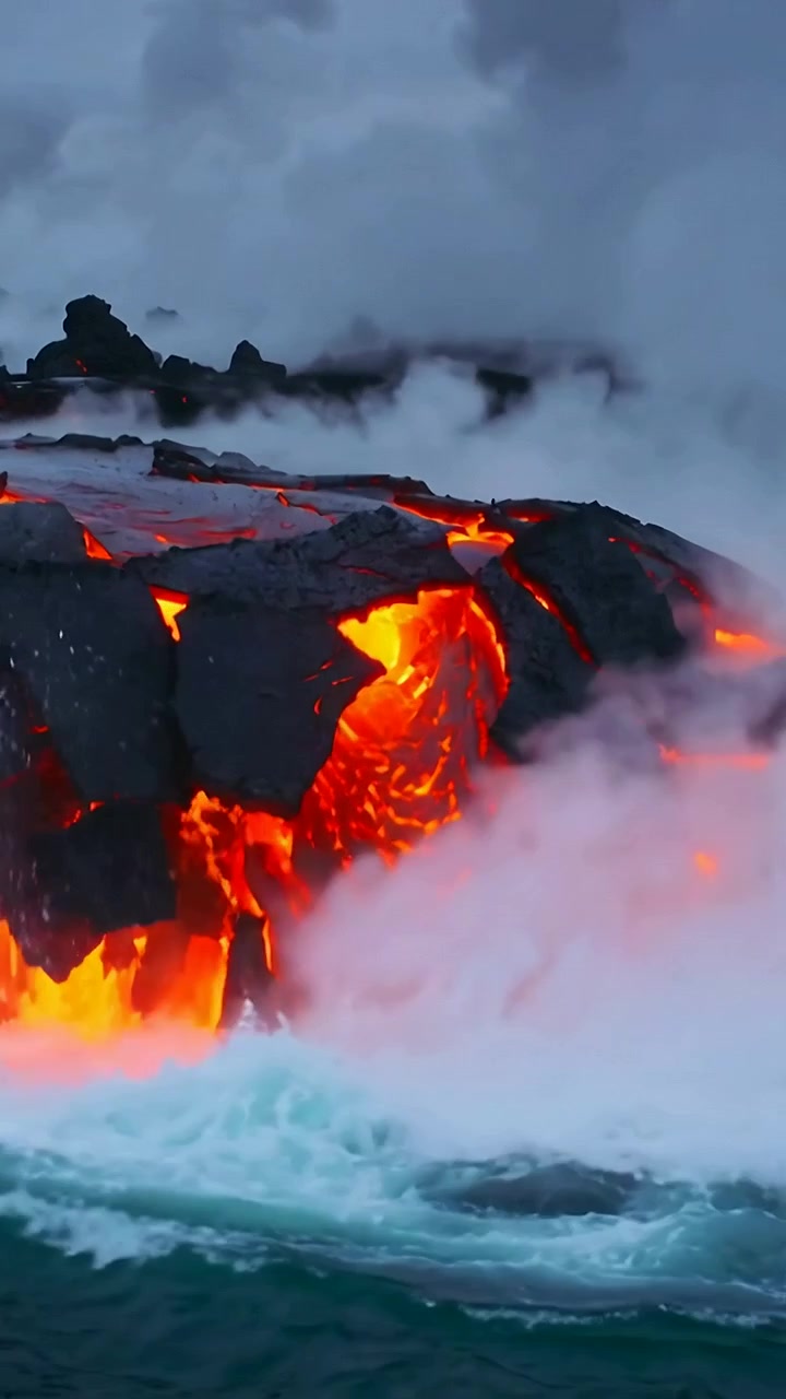 Vertical video: Pouring molten lava reaching cliff edge at rocky coast, creating steam and surf