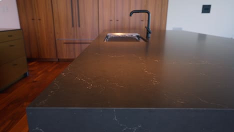 Toma-Panorámica-De-Una-Impresionante-Y-Espaciosa-Encimera-De-Granito-Negro-Adornada-Con-Un-Elegante-Grifo-Negro,-Creando-Un-Punto-Focal-De-Cocina-Elegante-Y-Moderno