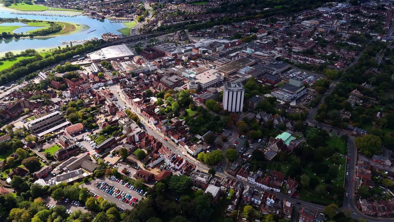 Aerial drone pans left over Fareham town centre with river and trees, showcasing cars, roads, and autumn colours glowing warmly in golden sunset light across the scenic English countryside
