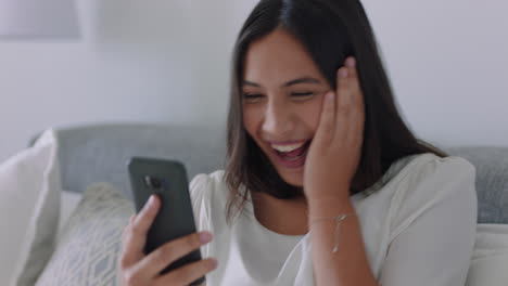 Hermosa-Mujer-De-Raza-Mixta-Teniendo-Video-Chat-Usando-Un-Teléfono-Inteligente-Que-Parece-Sorprendida-Disfrutando-De-Buenas-Noticias-Charlando-Por-Teléfono-Móvil-Relajándose-En-Casa