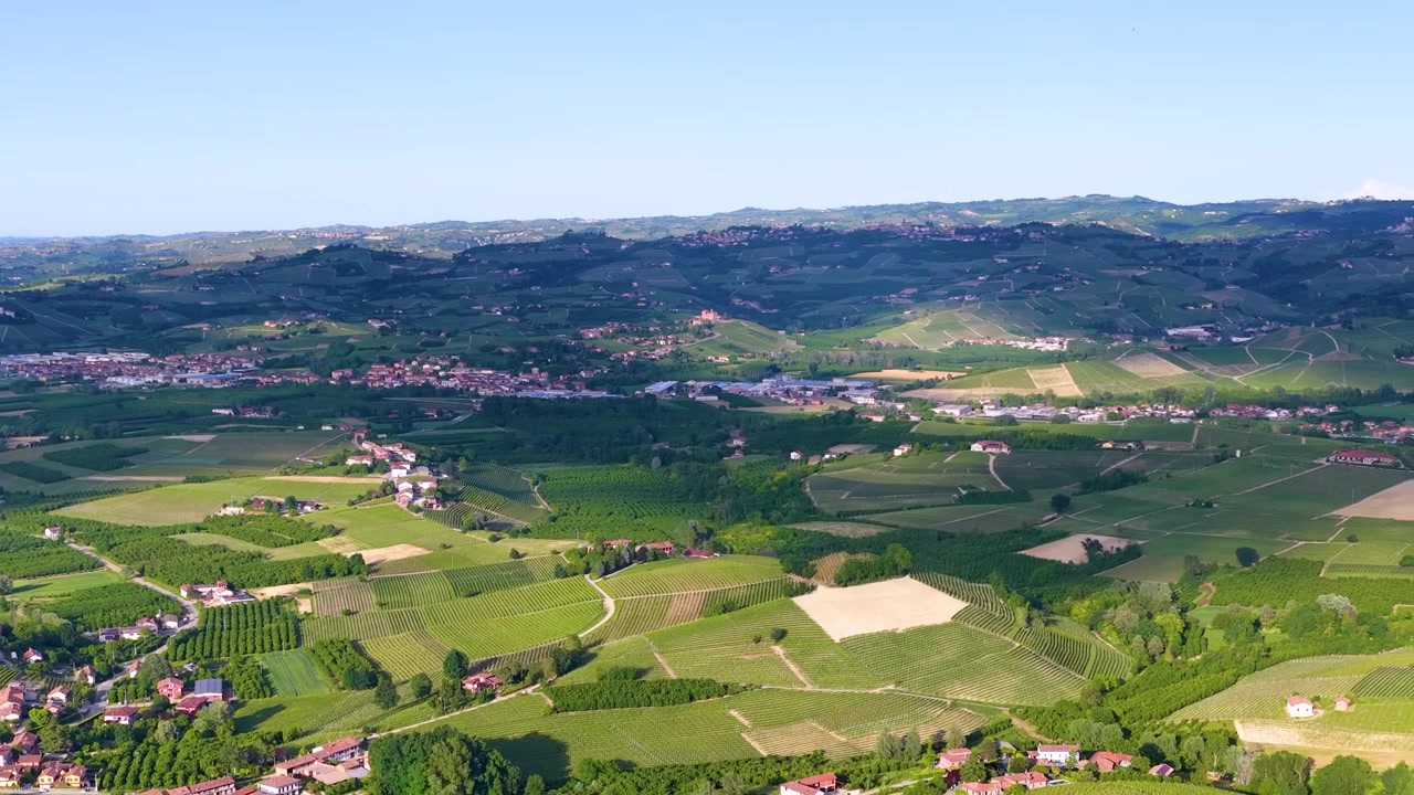 Brede luchtopname met drone die over weelderige groene wijngaarden en landelijke dorpen in Piemonte beweegt.