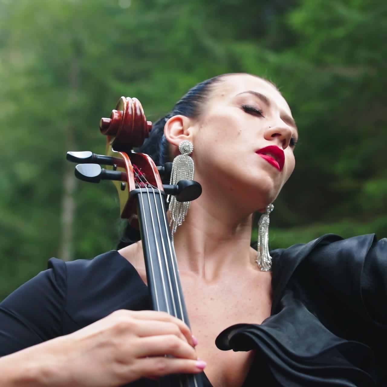 Passionate woman performs music. Attractive woman is playing the cello and enjoys the music by closing her eyes outdoors. Close-up.