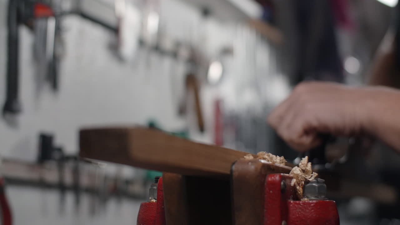 Close-up view of someone planing wood with a hand plane in a workshop