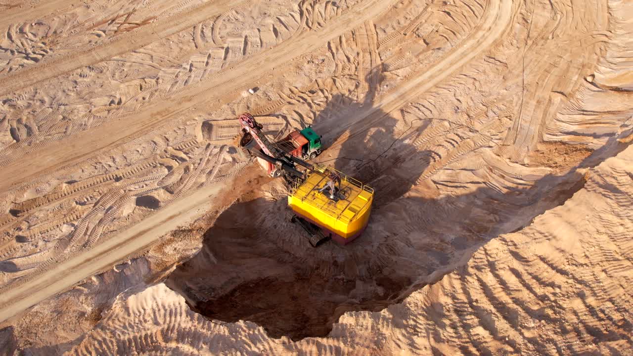 Electric rope shovel on sand mining in opencast. Mining excavator dropping rock ore into mine dump truck.