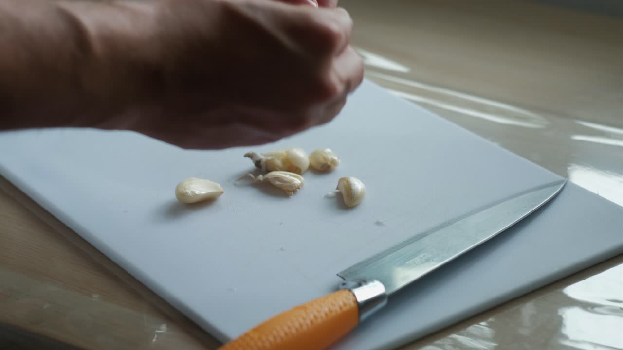Hands Peeling Cloves Of Garlic On Chopping Board In Kitchen. closeup shot