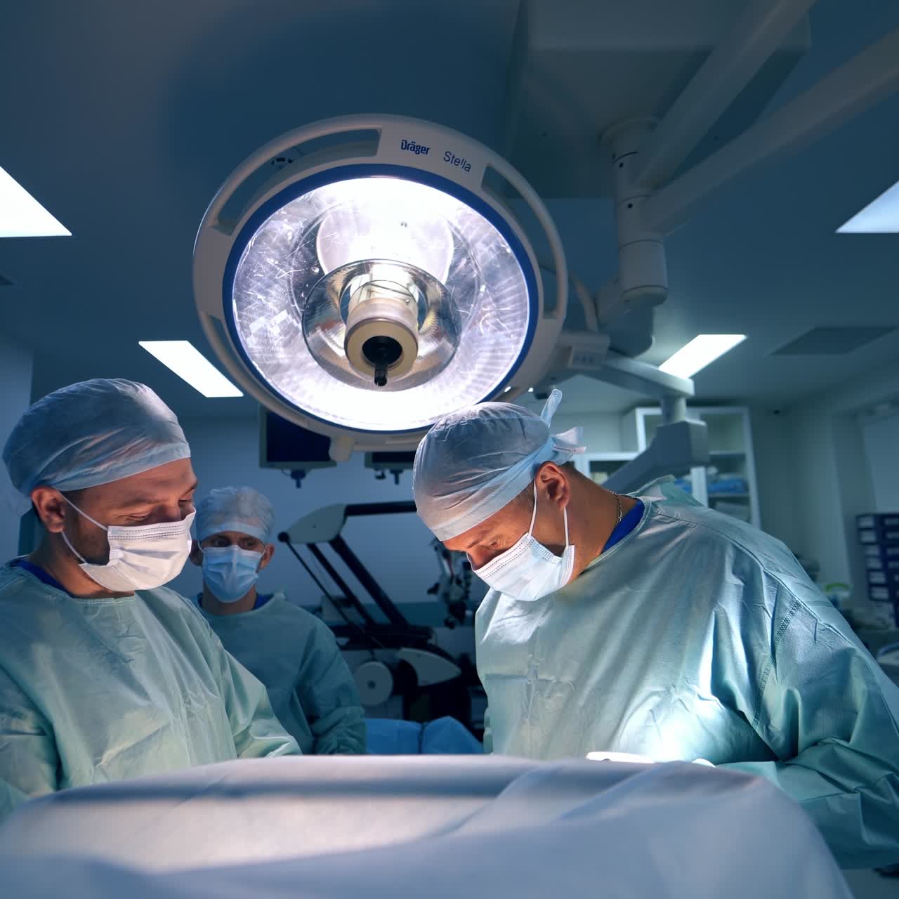 Two male surgeons performing operation in modern clinic. Male assistant standing at the background