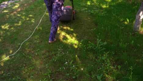 woman work with lawn mower. trimmer machine cutting green grass in the garden. garden work in summertime.