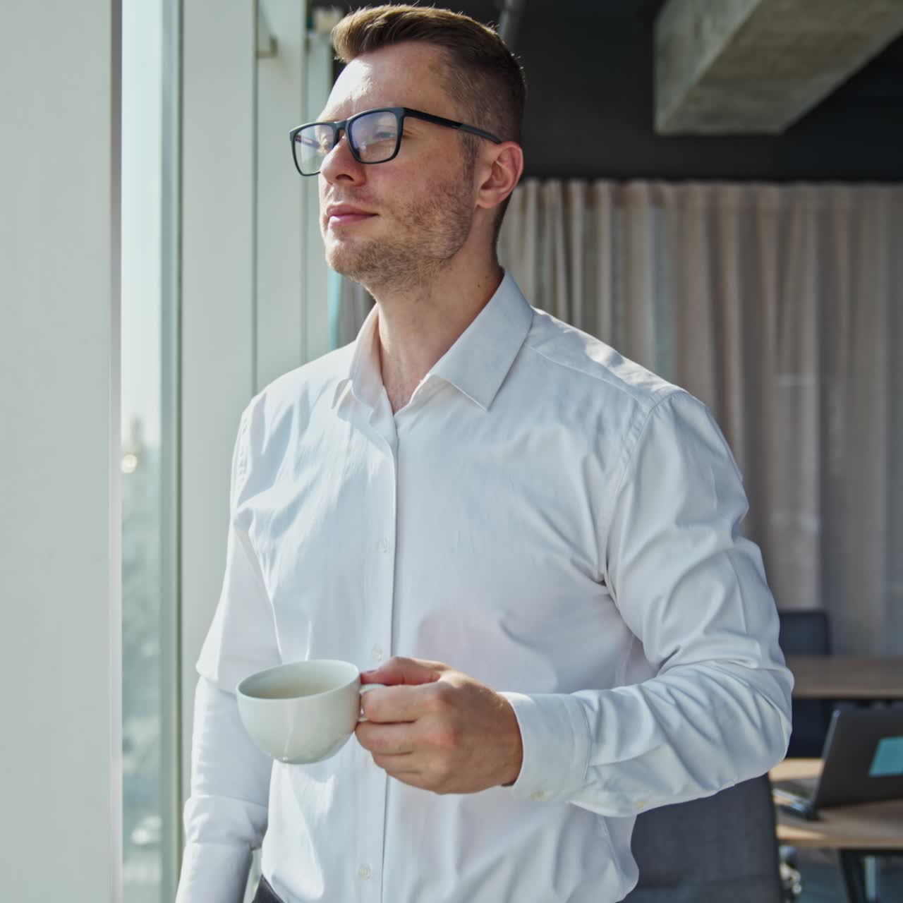 Imprenditore pensieroso e sicuro di sé beve caffè in piedi vicino alla finestra in ufficio. Uomo d'affari pranza ammirando la vista sulla città