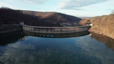 aerial reveal of the small town behind the dam, holding back the lake from the valley