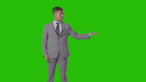 three quarter length shot of businessman in suit presenting or showing against green screen 1