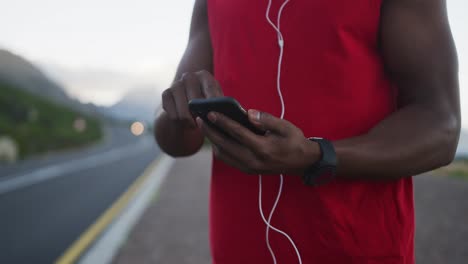 african american man wearing earphones using smartphone on the road