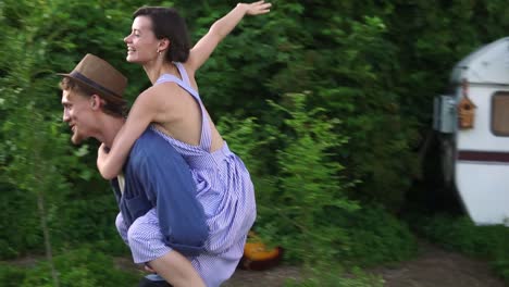 happy young lovely couple having fun near trailer in the park, man piggybacking girl, running happily, guy whirling her around. stylish, modern exterior