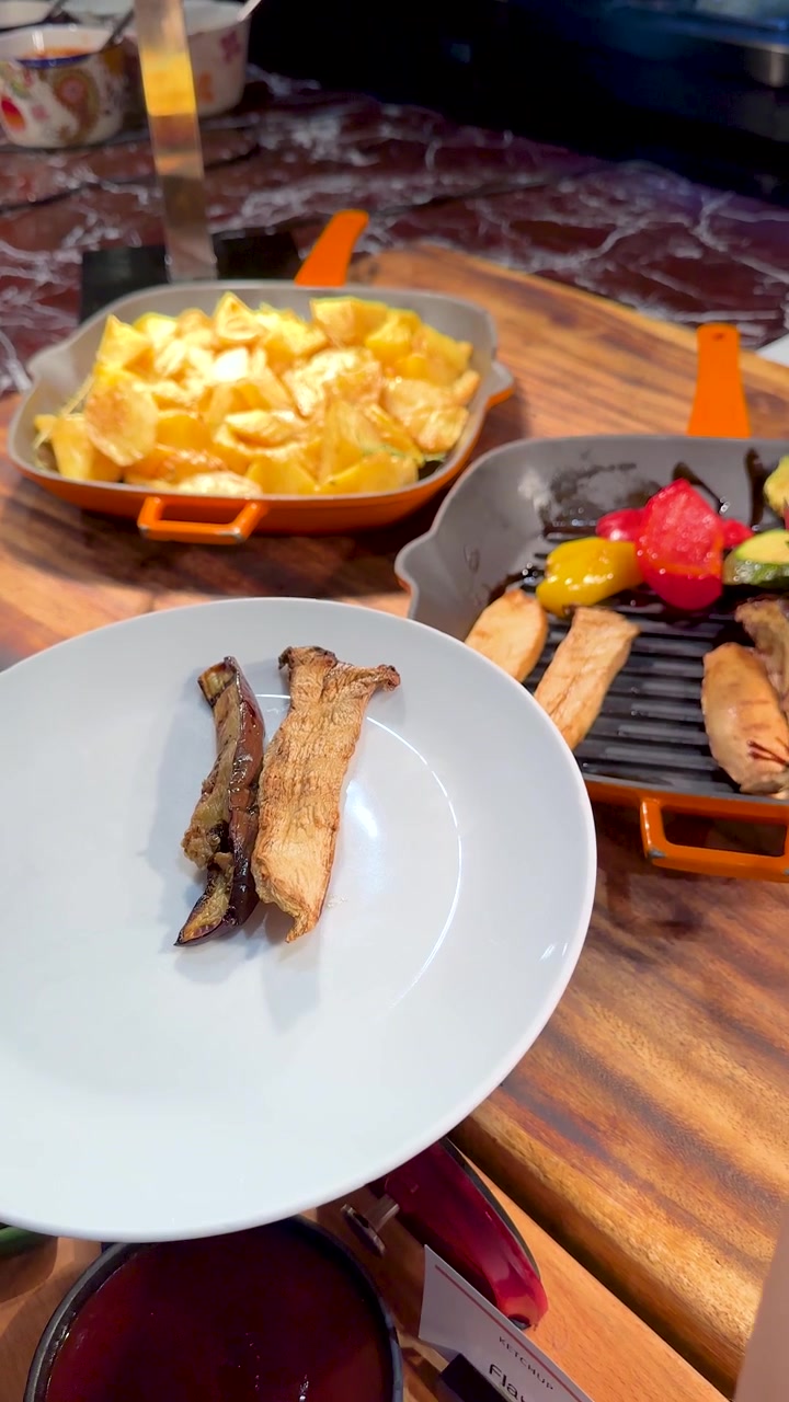 Primo piano di mani che usano le pinze per servire funghi e zucchine grigliati su un piatto.