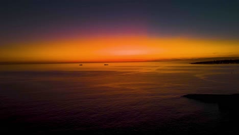 amazing yellow and orange sky after sunrise reflected on sea surface with some boats sailing in cascais