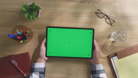 persona sosteniendo una tableta con una pantalla verde en un escritorio de madera