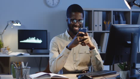 cheerful young man texting a message on the smartphone and smiling in the office at night