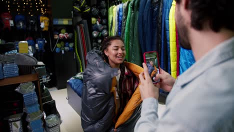 young couple choosing sleeping bag, a man makes photo of her girlfriend