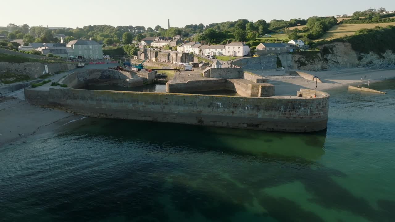 Approach to historic village harbour wall over clear blue sea. Charlestown, Cornwall, UK.