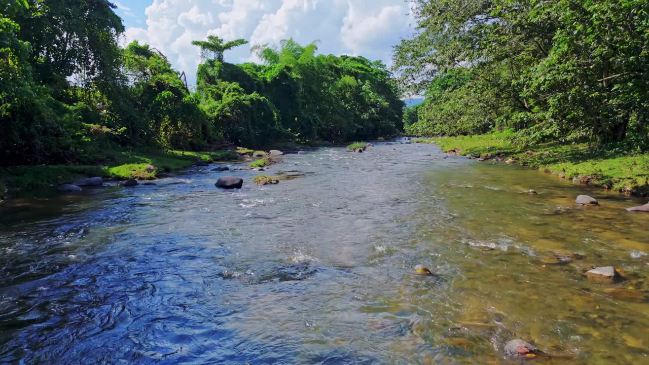 Aerial drone footage flying over rocky bed of Rio Maimon, surrounded by lush green tropical forest on sunny day, Dominican Republic