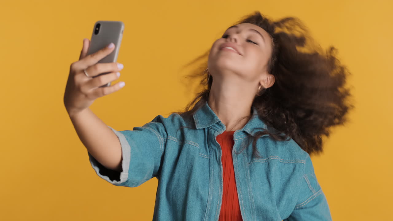 una mujer caucásica de cabello rizado tomando selfies con su teléfono inteligente.