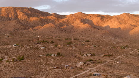 Flyover-beautiful-desert-landscape-in-Joshua-Tree,-California-with-houses-and-dirt-roads-in-the-foreground