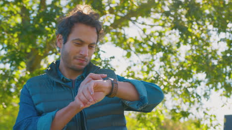 mature man standing by trees in autumn park looking at smart watch