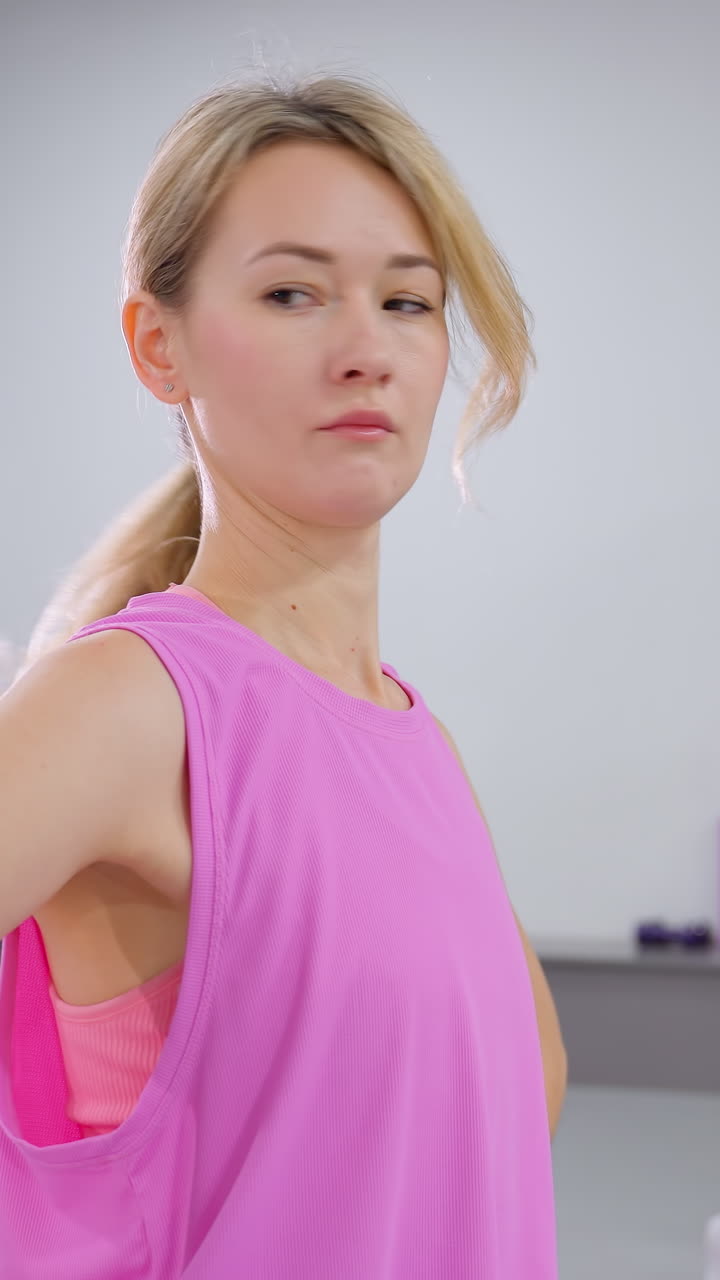 молодая женщина в розовом тренируется с другом в коричневом наряде, сосредотачиваясь на упражнениях на растяжку в яркой среде тренажерного зала, отражение в зеркале и фитнес-оборудование, видимые на заднем плане