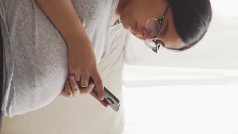 mujer embarazada morena con gafas sentada escribiendo en un teléfono móvil