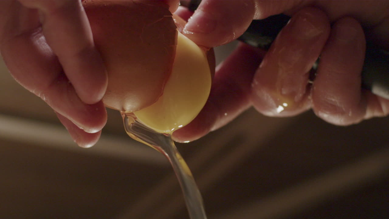 A person hands cracking open a egg with egg white and yellow yolk pouring out in slow motion, close up