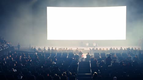 large audience watching a presentation with a blank screen on stage, creating an atmosphere of anticipation and curiosity