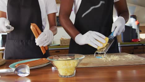 sección media de una pareja afroamericana con delantales preparando perritos calientes juntos en el camión de comida