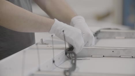 close-up of two hands in white gloves carefully connecting a wire to a board using cable ties in a documentary-style handheld shot, all in focus