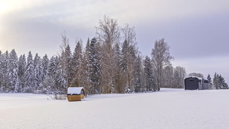 Lapso-De-Tiempo-Del-Hermoso-Paisaje-Invernal-Con-Nubes-Voladoras-Y-Luz-Solar-En-El-Cielo---Sauna-De-Barril-Y-Casa-De-Madera-En-Un-Campo-Nevado-Frente-A-Abetos-Blancos