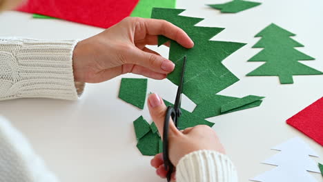 woman hands cut out a christmas tree of green fabric with scissors