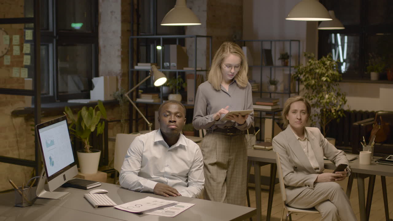 American Man Employee And Female Coworker Sitting On A Chair And Looking At Camera In The Office
