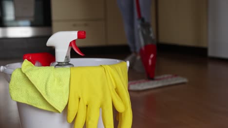 4k video footage detergents in a bucket on the floor and woman cleaning her home in the background