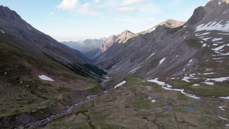 aerial drone footage facing down a glacial valley and slowly reverseing through a dramatic, jagged mountain landscape with residual patches of snow and alpine meadows in switzerland