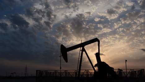 silhouette of crude oil pump standing still in the oilfield at cloudy sunset