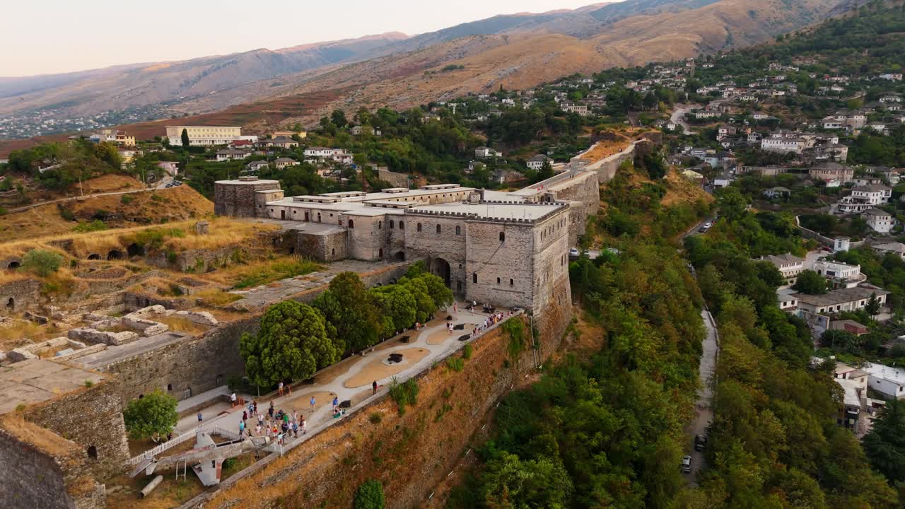 castillo de gjastirokër y ciudad de la ladera con árboles verdes exuberantes y montañas lejanas al atardecer