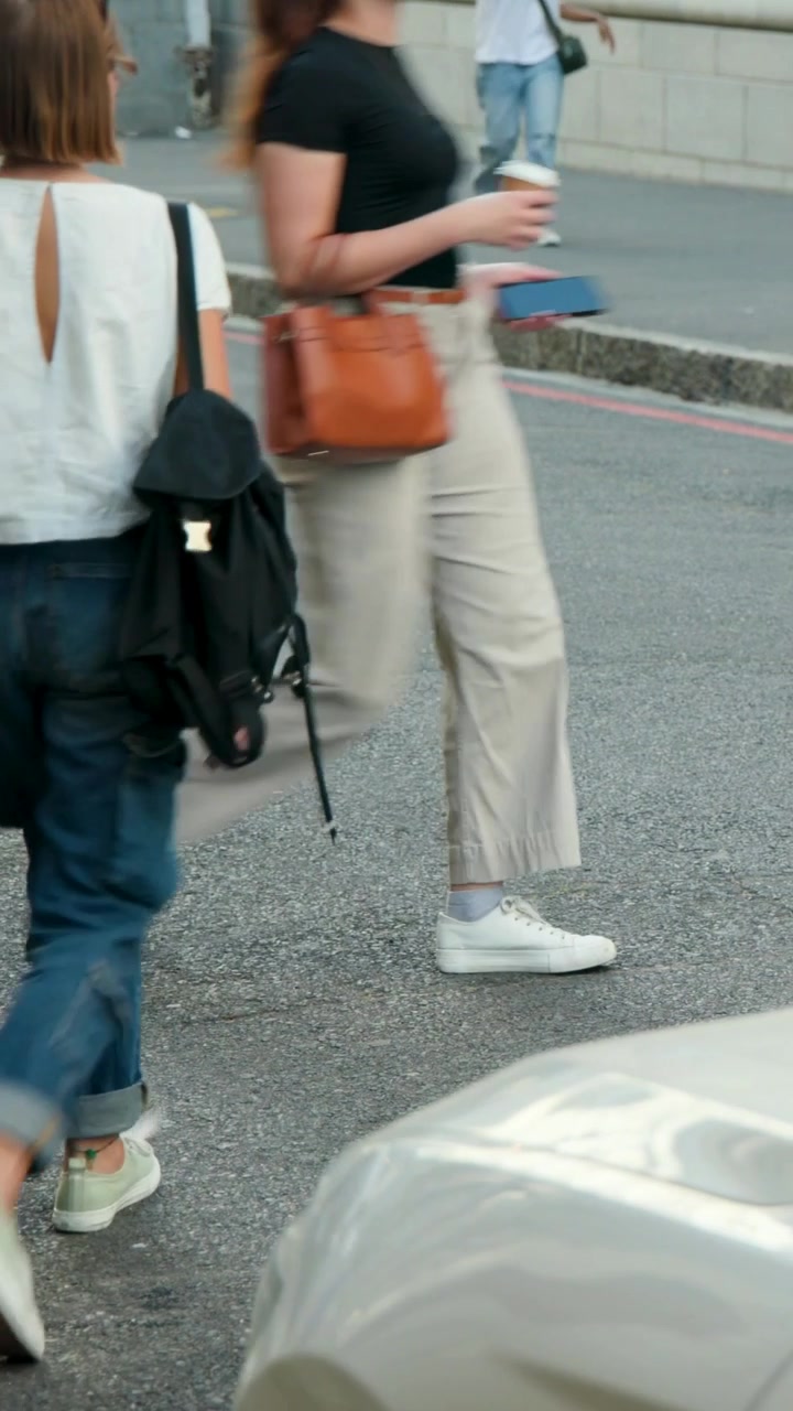 Vertical video: Stepping woman white top, rolled jeans crossing street off curb with black backpack