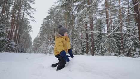 cute little boy is playing with snow in forest in winter day happy toddler in warm jacket smiling