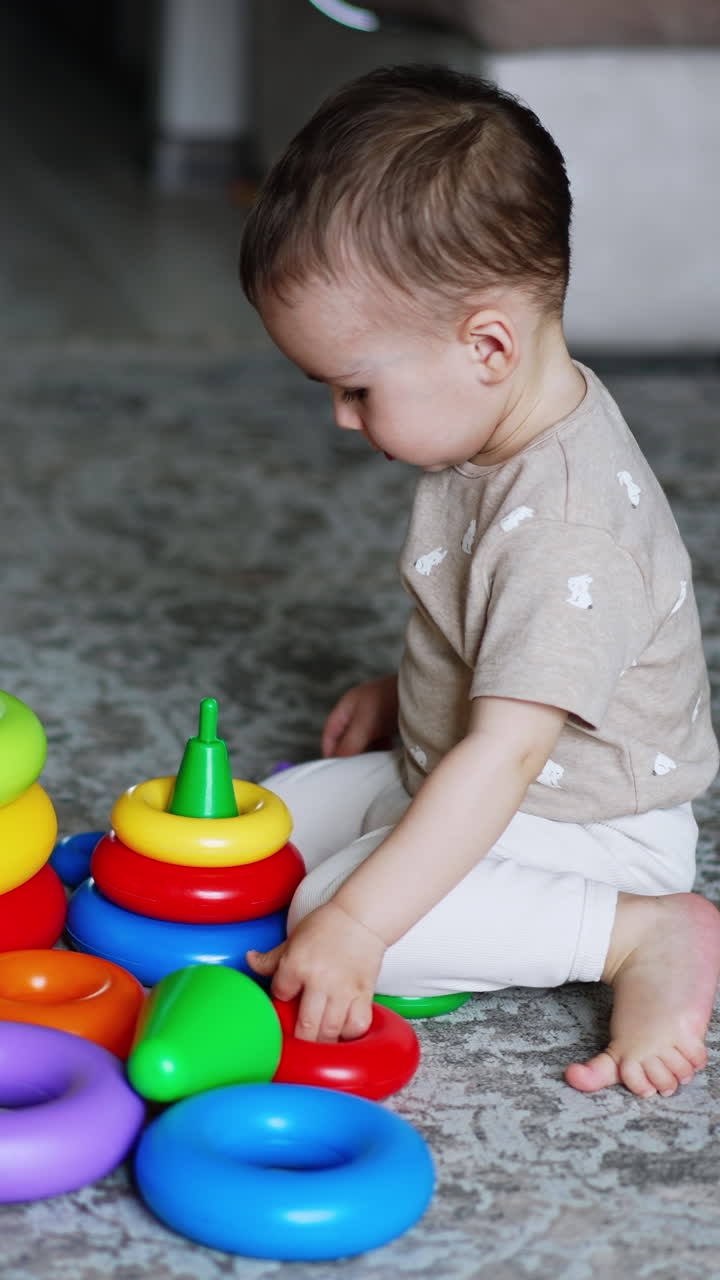 Smart little boy plays with his toys on the floor. Lovely baby assembling the pyramids. High angle view. Vertical video