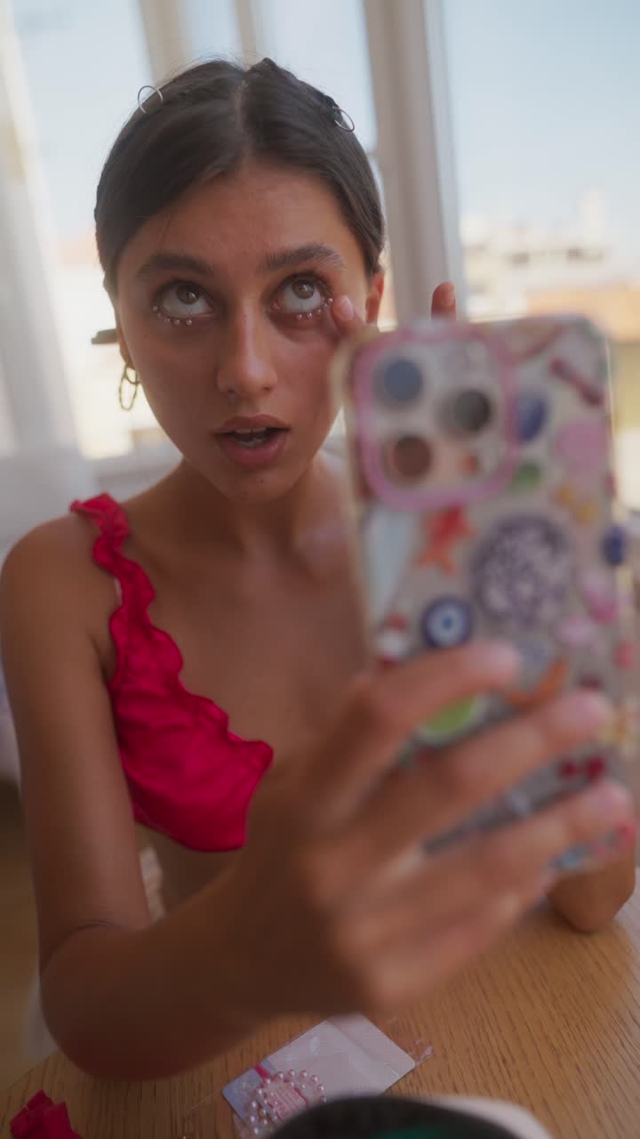 Young woman applying face beads while looking at her phone