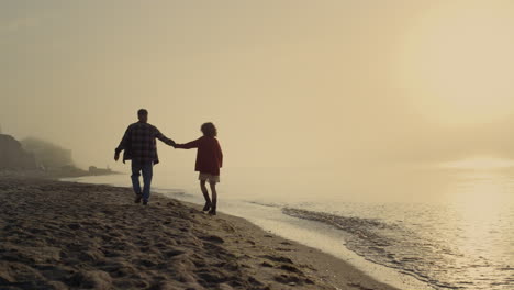 Glückliche-Frau-Und-Mann,-Die-Am-Meeresstrand-Spazieren-Gehen.-Hübsches-Paar,-Das-Sich-Bei-Sonnenaufgang-An-Den-Händen-Hält