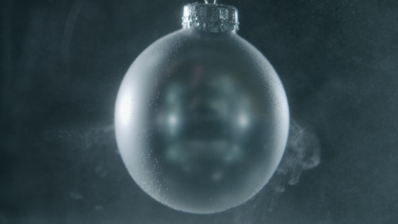 Silberne Christbaumkugel dreht sich langsam in dunkler Umgebung.